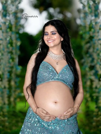 A joyful bare-bump portrait in our outdoor setting. The mother-to-be is wearing a sparkling blue two-piece lehenga, celebrating her pregnancy with confidence and style.