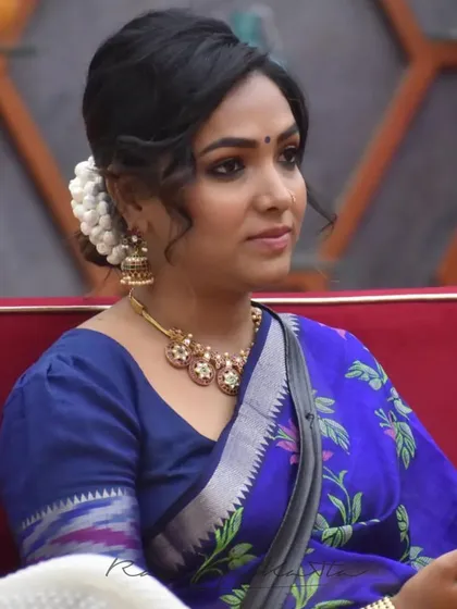 A close-up of Anupama Gowda in the mustard and indigo half saree, showcasing the elegant puff-sleeved blouse and traditional jewelry.