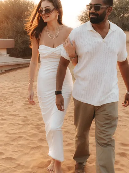 A stylish walk through the desert at golden hour. The warm light, flowing dress, and linked arms create a chic and romantic candid photograph.