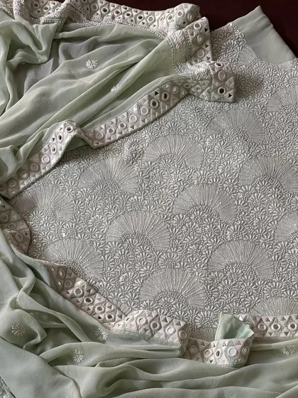 Experience modern elegance with our Mint Green suit in pure georgette. The fabric is adorned with a heavy 'Teen Taar' Chikankari jaal, which is further illuminated by Poth, Kutdana, and a handcrafted Kutchi mirrorwork border for a touch of refined glamour.