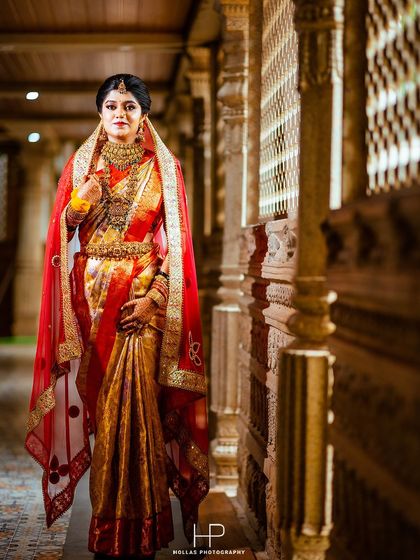 A full-length portrait of the bride in her stunning red and gold wedding saree.