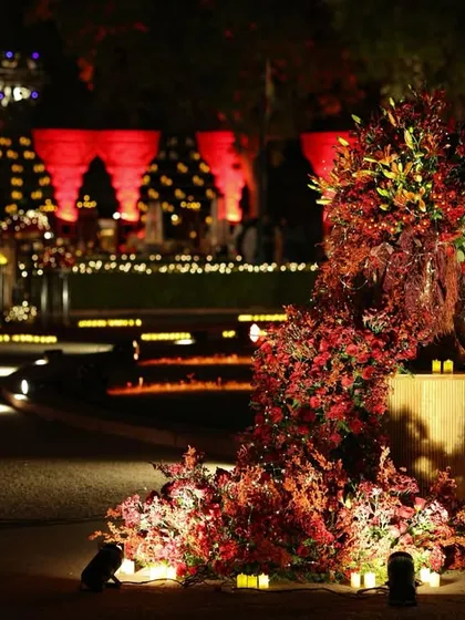 A dramatic floral installation cascades down a wooden pedestal, surrounded by candles, creating a stunning piece of decor for the outdoor event space.