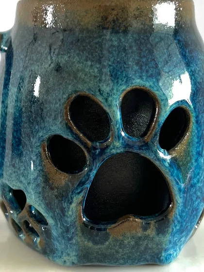 A detailed shot of the paw print carving. The glossy blue glaze pools inside the deep impressions, creating a beautiful contrast with the raised parts of the design.