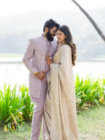 A romantic, full-length shot of the couple by the water. This view shows how their coordinated pastel outfits create a soft, dreamy, and sophisticated aesthetic for their reception.