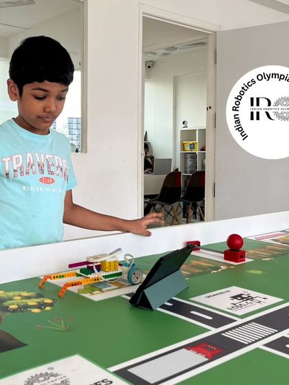 An IRO trainee tests his robot on the "Harvest Heroes" challenge mat. He is programming the robot to interact with specific game elements related to farming tasks.