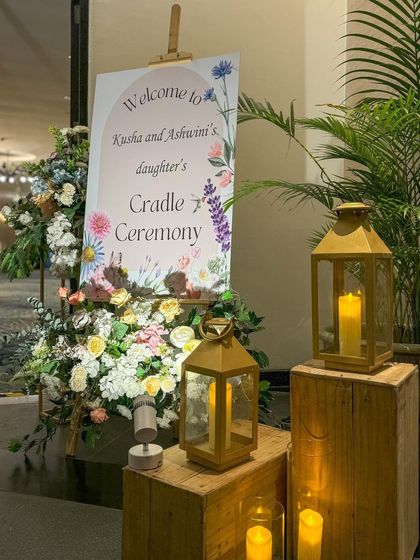 A beautiful welcome sign for a cradle ceremony, adorned with wildflowers and flanked by candle-lit lanterns.