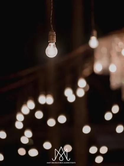A beautiful shot focusing on the hanging Edison bulbs and a distant chandelier, showcasing the layered lighting design that created this magical ambiance.