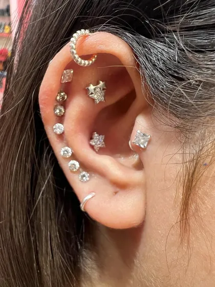 A fully curated ear with a mix of gold and silver pieces, including a crescent hoop, star studs, and solitaires.