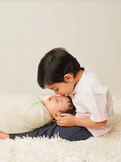 A close-up of a big brother's kiss. The simple white background keeps the focus entirely on this heartwarming moment.