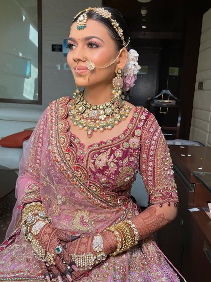 A royal bride in a deep pink lehenga. Her hair is styled in a classic updo, adorned with flowers, to match her majestic outfit.