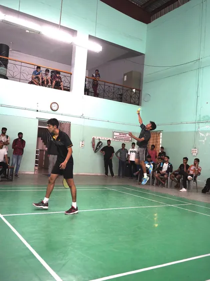 A doubles match in progress, with one player airborne and executing a smash while his partner holds his position.