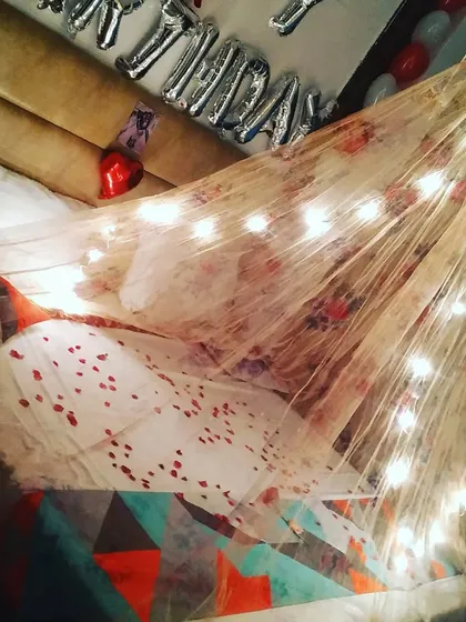 For a cozy and dreamy atmosphere, I create beautiful bed canopies using sheer fabric and warm fairy lights. This setup, complete with scattered petals, turns any bed into a romantic focal point for an anniversary or surprise.