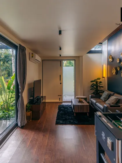 The living room of a 2BHK cargo home, featuring rich hardwood floors and a dark accent wall with gold decorative plates. The space is designed to be both stylish and comfortable, with a foosball table for entertainment.