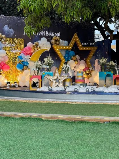 A "Twinkle Twinkle Little Star" theme for a twin's birthday party. The stage is set with a night-sky backdrop, a gold sequin wall, and large marquee stars and a moon, creating a magical celestial scene.