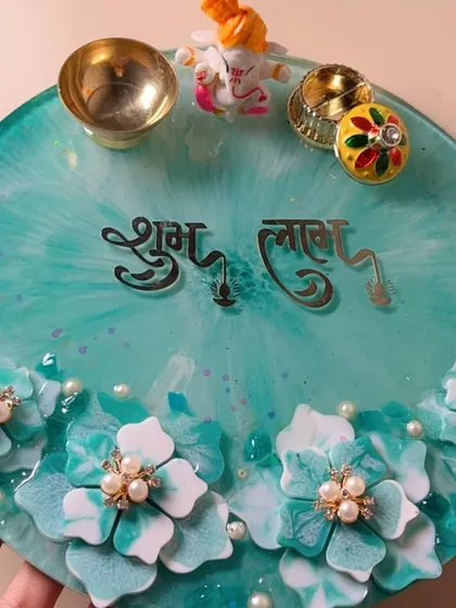 Make your festive occasions even more special with a custom pooja thali. This 10-inch resin thali is designed in a beautiful sea-green with hand-sculpted 3D flowers, pearl details, and "Shubh Labh" lettering. It comes complete with a Ganesha idol, a diya, and a kumkum holder.