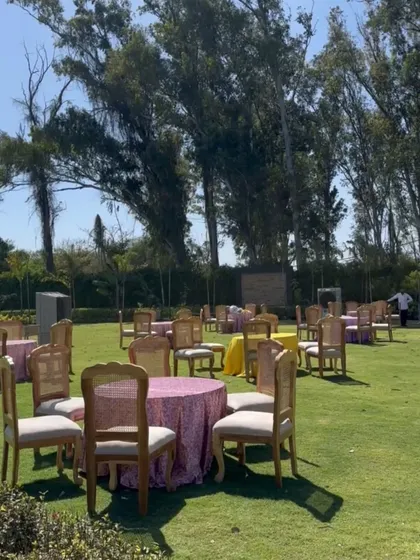 Simple and elegant outdoor seating for a daytime Haldi function, with pink and yellow tablecloths adding a pop of color to the green lawn.