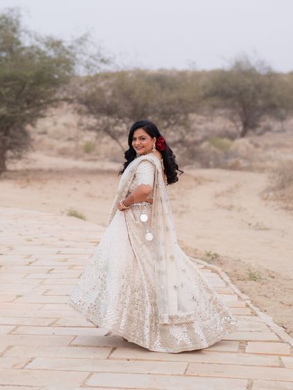 The bride's full look, her ivory lehenga with mirror work sparkling against the rustic desert landscape.