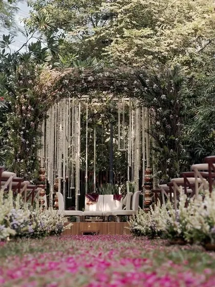 The view down the aisle, strewn with petals, leading to a mandap that blends seamlessly with the surrounding greenery.