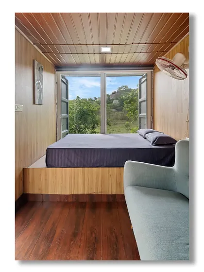 The bedroom of 'The Boulder Nest,' where a large window frames a beautiful view of the surrounding landscape. The elevated bed and simple decor create a serene and minimalist sleeping space.