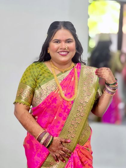 A happy client in a bright pink and green saree. Her hair is styled with a simple center part and soft waves, a classic look for any occasion.
