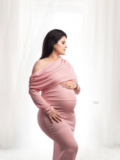 A serene and contemplative portrait. The soft side lighting from the window beautifully illuminates the client's profile and her form-fitting pink gown.