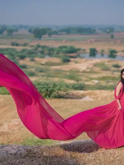 The rani pink georgette trail gown flowing in the wind against a rustic, natural backdrop. The movement in the trail adds a beautiful, dynamic element to the photograph.