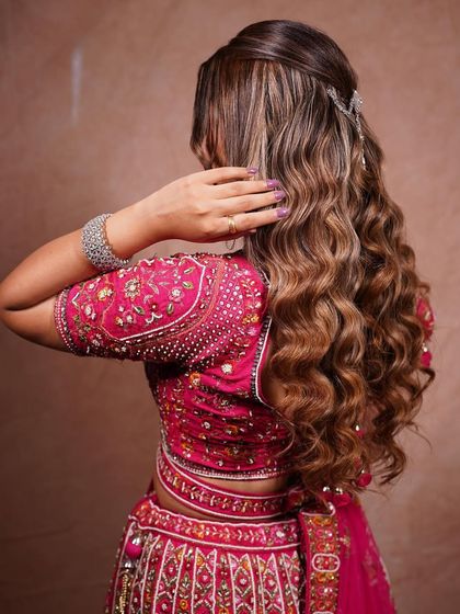 A back view of glamorous waves for a reception or sangeet look. The hair is styled into deep, uniform waves and given a beautiful shine, with a simple clip to hold the half-up style in place.