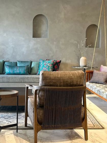 This living space is defined by its textures and tones. A concrete-finish sofa base, a traditional wooden swing, and soft woven armchairs come together to create a room that feels both contemporary and deeply rooted.