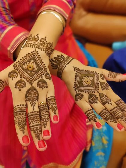 A modern and geometric take on the lotus motif. The flower is enclosed in a diamond shape with hanging jhumkas, creating a chic and symmetrical design on the back of the hands.