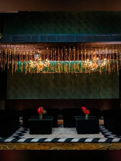 A chic lounge area for a cocktail night. The decor features a stunning chandelier installation with hanging crystals over plush black sofas, creating an elegant and comfortable space for guests.