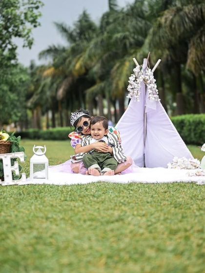A sweet moment between siblings during an outdoor photoshoot. The older sister gives her baby brother a hug in front of the birthday teepee setup.