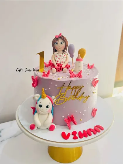 A one-derful first birthday cake with a fondant doll and her unicorn friend, decorated with whimsical butterflies.