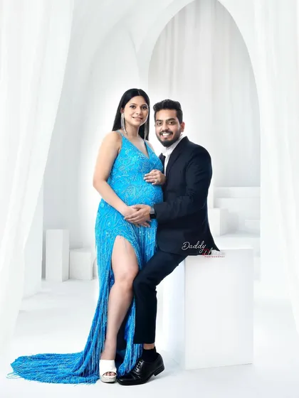 A glamorous couple's portrait in my studio. The expectant mother shines in a sparkling blue sequin gown, showcasing the variety of high-end outfits available in my luxury wardrobe collection.