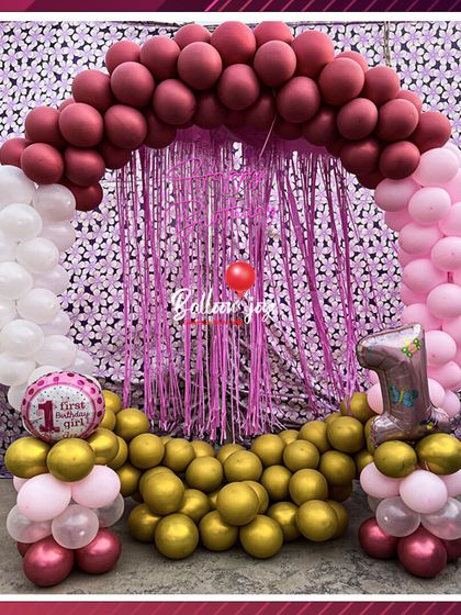 Pretty in pink for a first birthday girl! This lovely balloon arch combines shades of pink, white, and gold with a shimmering curtain backdrop, creating a classic and celebratory photo spot.