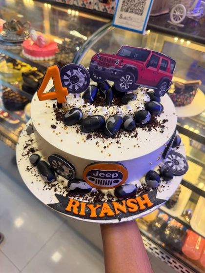 This Jeep-themed cake is perfect for an off-road adventure lover. It features a red Jeep topper, edible rocks, and tire details, celebrating a 4th birthday with a rugged and fun design.