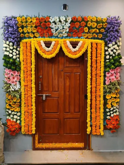 This doorway is decorated with a full frame of colorful flowers, including marigold garlands, purple orchids, and white and pink asters, creating a rich, multi-layered traditional look for a festive occasion.