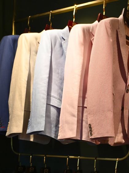 A rack of our tailored blazers in various lightweight fabrics and colors, including linen and seersucker. This collection is designed for refined casual wear, perfect for warmer climates.