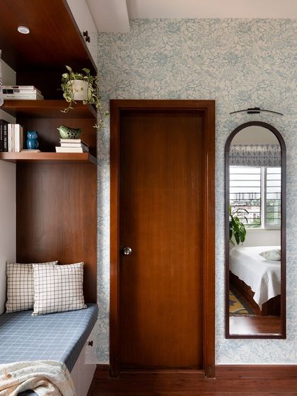 An arched mirror and a bay window seating nook with patterned wallpaper create a cozy and charming corner in this bedroom.