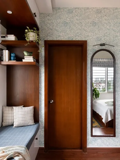 An arched mirror and a bay window seating nook with patterned wallpaper create a cozy and charming corner in this bedroom.