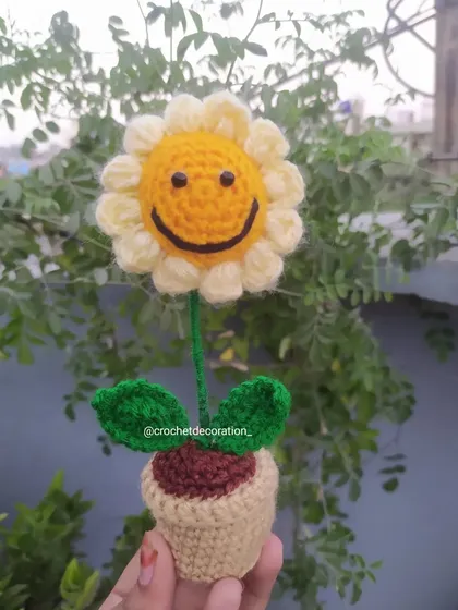 Another view of the smiley sunflower pot, held against a natural green background.