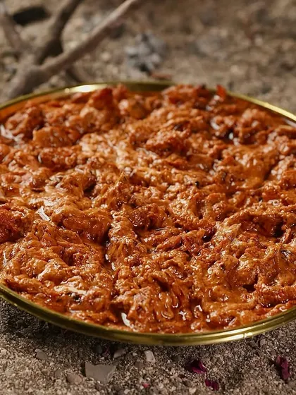 A tighter shot of the Shahi Butter Chicken, showcasing the thick, luscious texture of the gravy and the generous amount of shredded chicken.