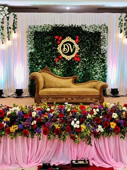 An elegant and classic reception stage combining a rich floral border with a modern green wall backdrop. We added a personalized, illuminated monogram for the couple, 'DV', making the design truly unique to their story.