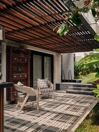 The outdoor deck area features a patterned tile floor and comfortable seating, surrounded by lush greenery. An antique carved door adds a touch of traditional charm to this modern space.