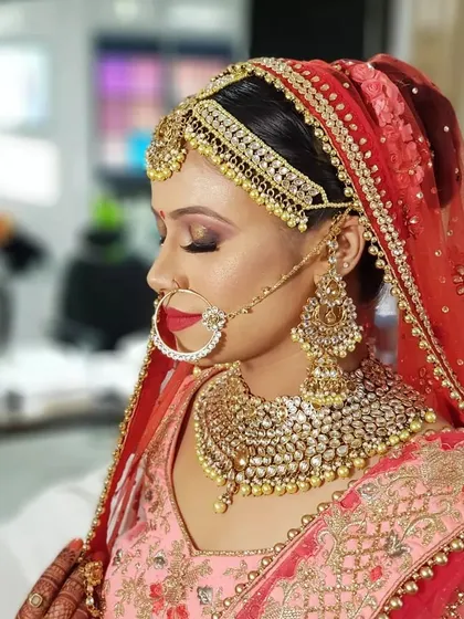 A side profile showcasing the intricate details of the bridal look. You can see the heavy Kundan jewelry, the matha patti, and the dramatic eye makeup with a pop of red on the lips.