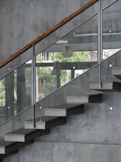 A detail of the cantilevered stairs, showcasing the clean joinery between the concrete treads, glass railing, and wooden handrail.