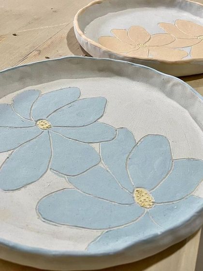 Two beautiful plates painted with floral designs, showcasing the slip-trailing and painting techniques taught in our workshops.