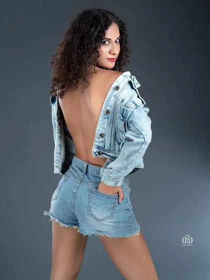 This backless denim-on-denim look is captured in the studio against a simple grey backdrop. The focus is on the casual yet confident pose and the texture of the fabric, creating a classic and timeless fashion portrait.