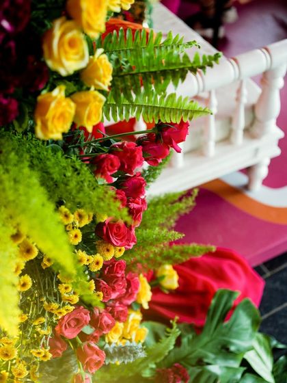 A close-up of a floral arrangement, showing the fresh ferns, red and yellow roses, and the white balustrade of the seating.
