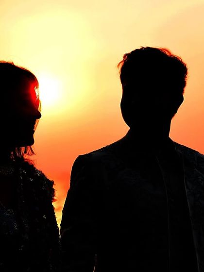 A powerful silhouette of a couple against a fiery orange sunset over the ocean. This dramatic lighting creates a striking and artistic pre-wedding portrait that focuses on their profiles.