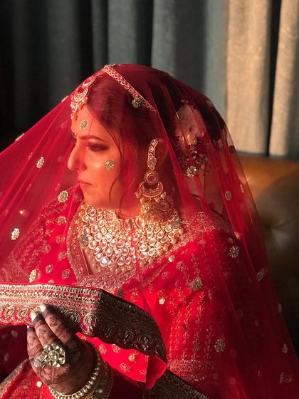 A side profile showing the intricate floral arrangement on the bun, a timeless choice for a traditional red bridal lehenga.